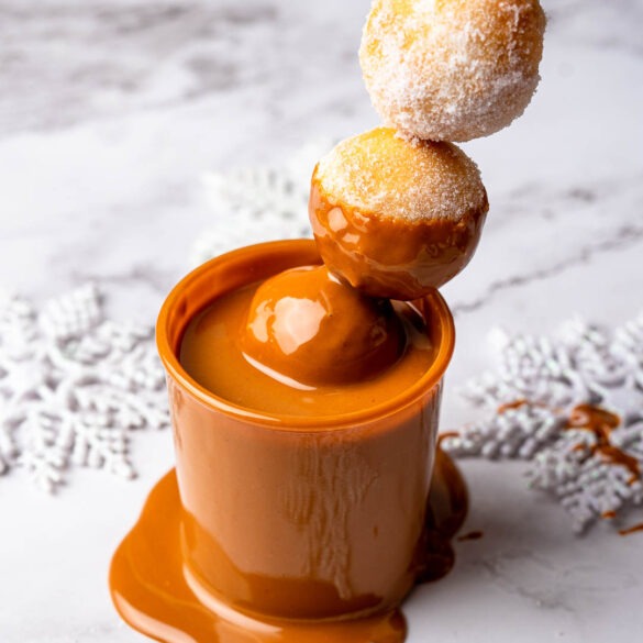 Doughnut balls on a stick, dipped in a cup go biscoff sauce.