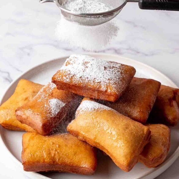 Icing sugar dusted over beignets piled on top of each other on a plate.