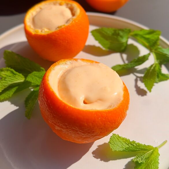Aperol spritz ice cream in orange cups on a plate with mint leaves.