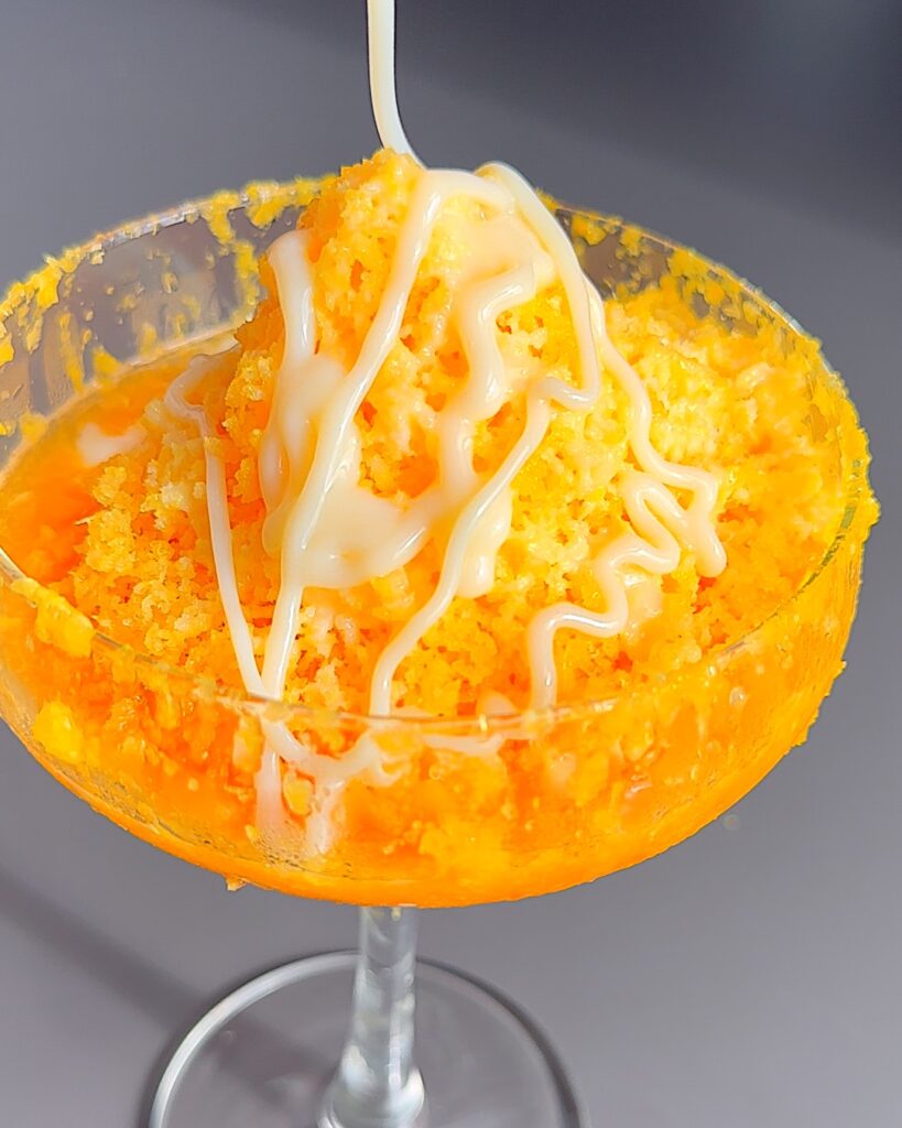 Condensed milk drizzled on top of grated frozen orange in a cocktail glass.