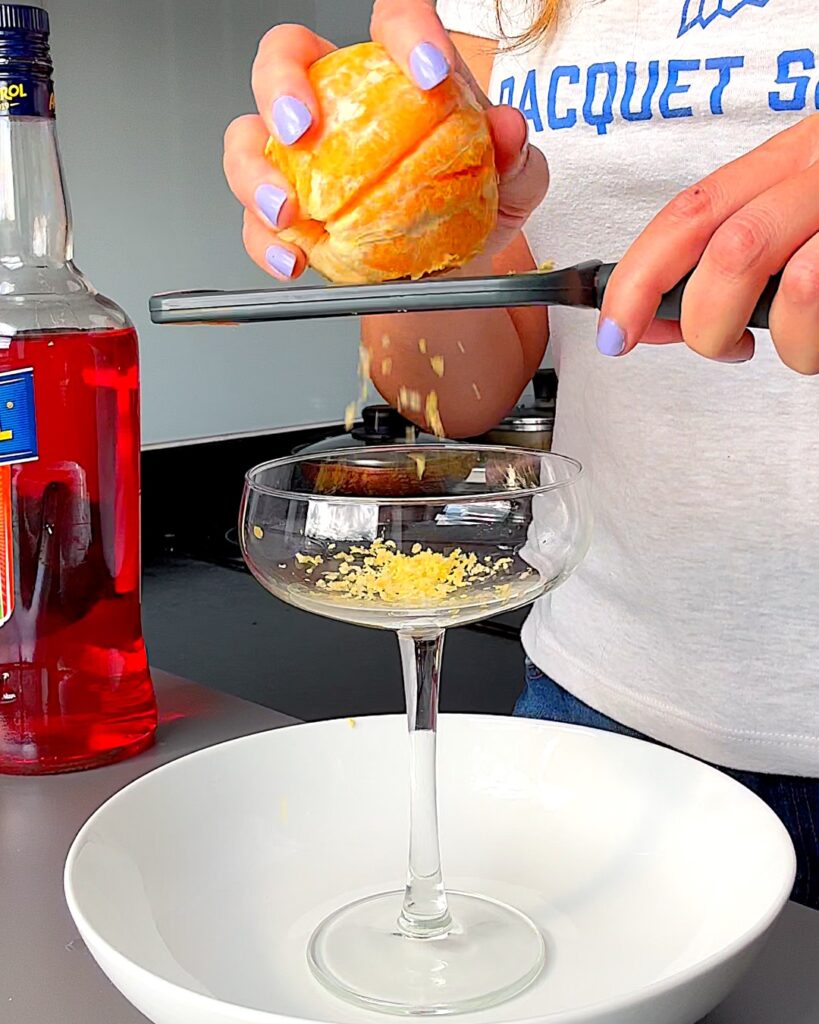 A frozen orange being grated into a cocktail glass.