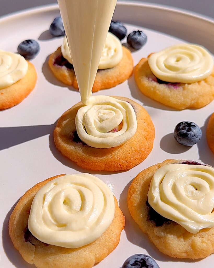 Cheesecake filling piped on top of a mini blueberry cookie.