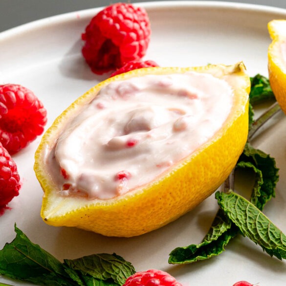 Lemon and raspberry ice cream in a lemon cup on a plate with mint leaves and raspberries.