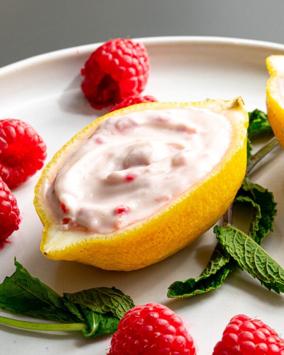Lemon and raspberry ice cream in a lemon cup on a plate with mint leaves and raspberries.