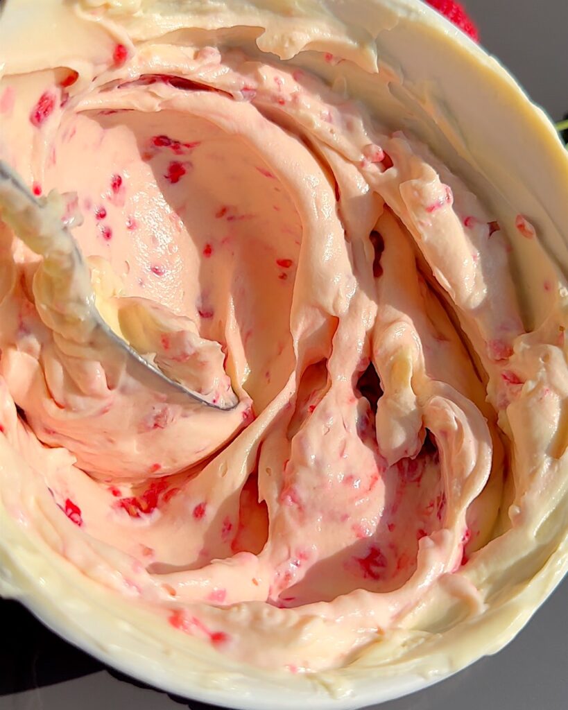 Raspberries mixed being mixed into creamy ice cream mix in a bowl.