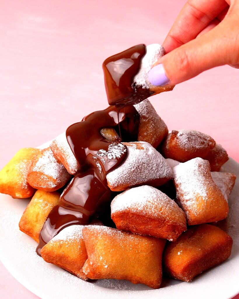 Pile of mini Beignets with melted chocolate drizzled on top.