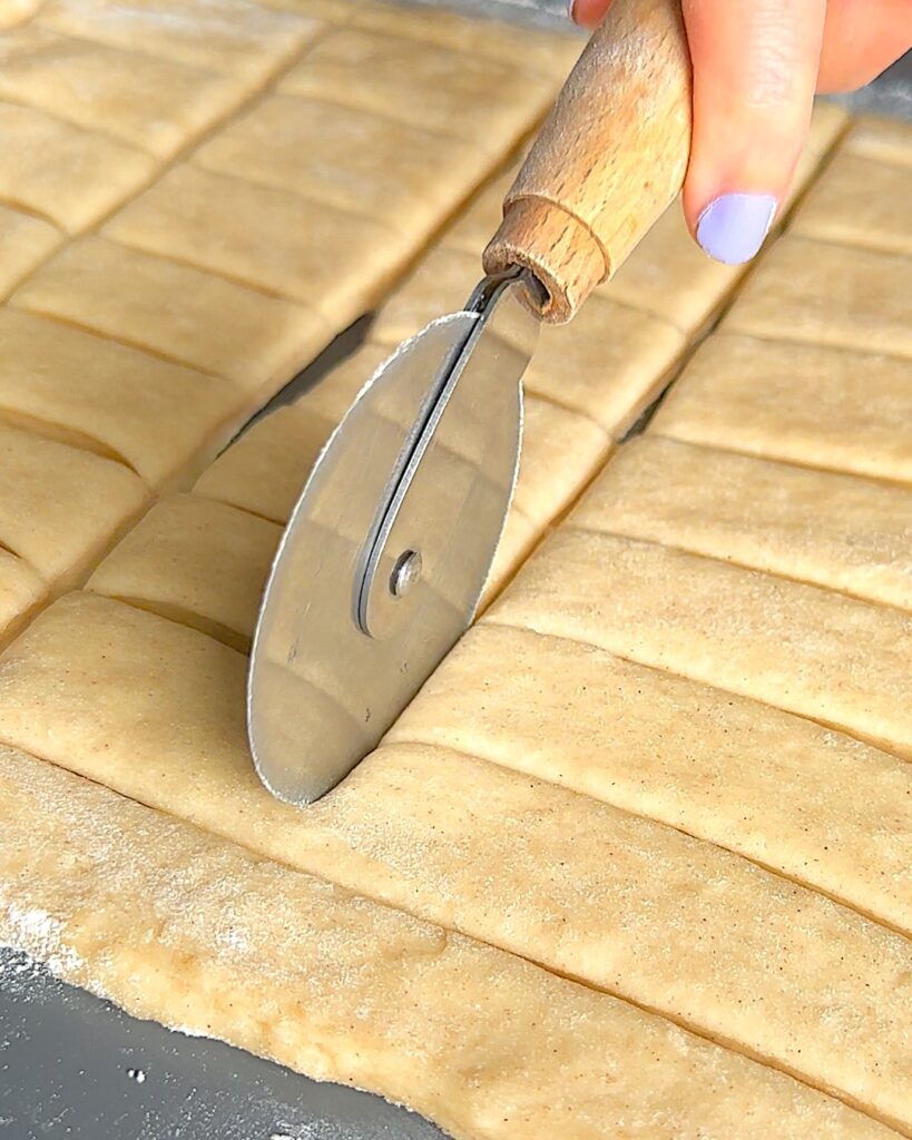 Beignet dough being cut into rectangles with a pizza cutter.