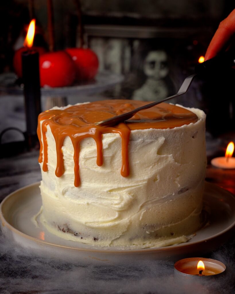 Caramel sauce dripping down the side of a cake covered in vanilla buttercream.