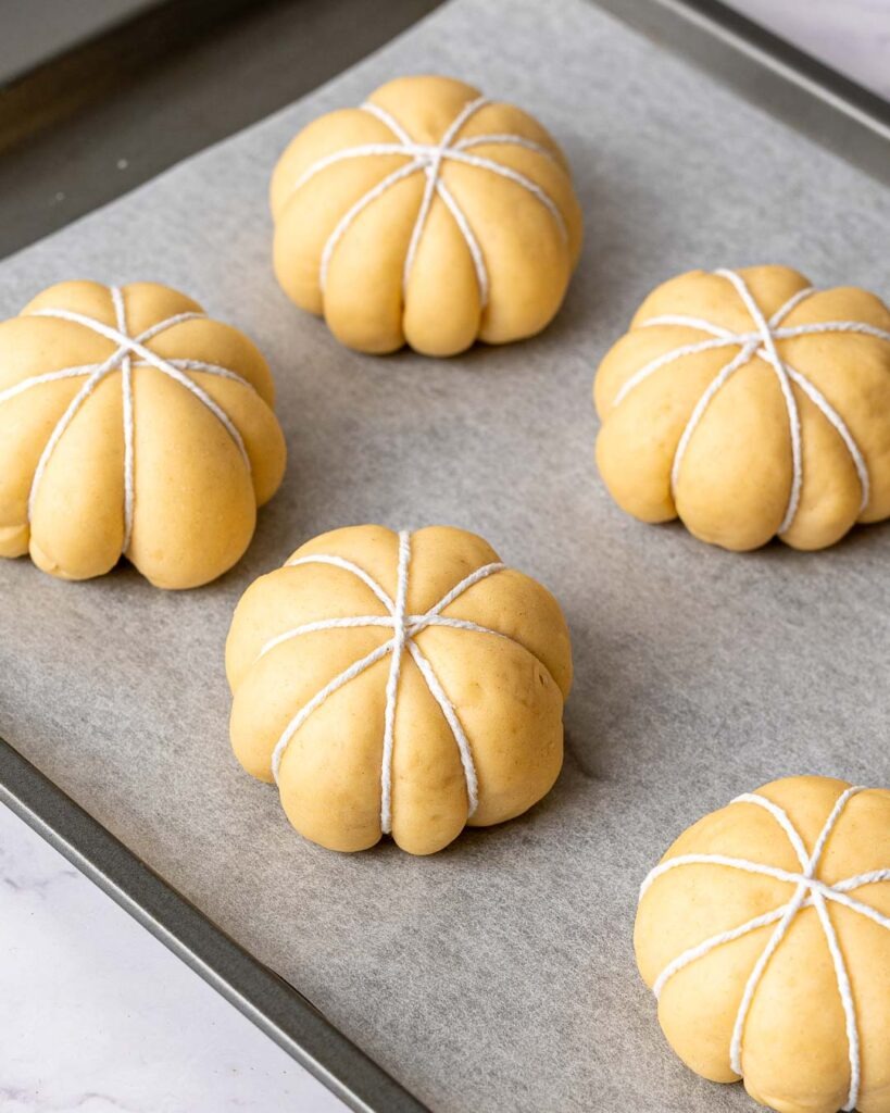 Pumpkin shaped buns wrapped in string on a baking tray before going in the oven.
