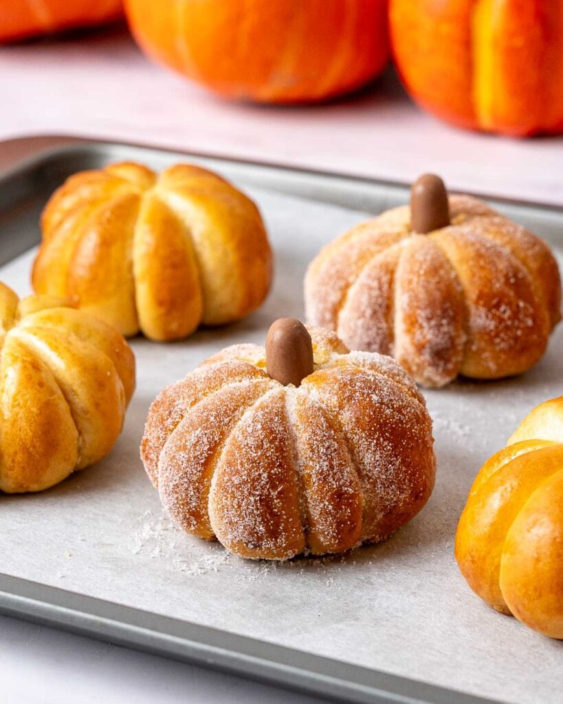 Pumpkin shaped buns covered in sugar on a baking tray.