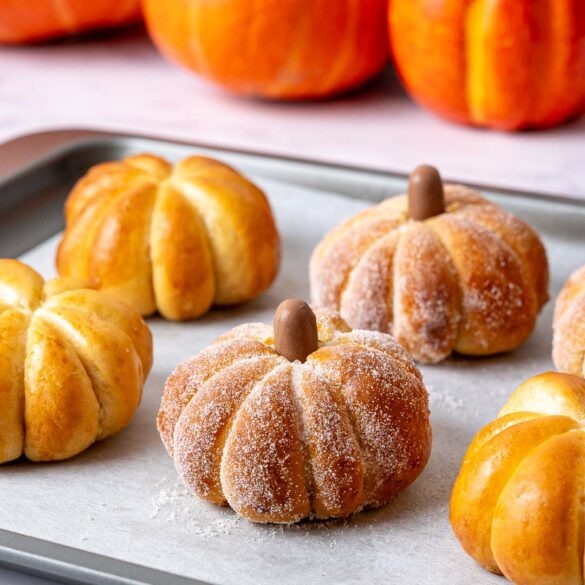 Pumpkin shaped buns covered in sugar on a baking tray.