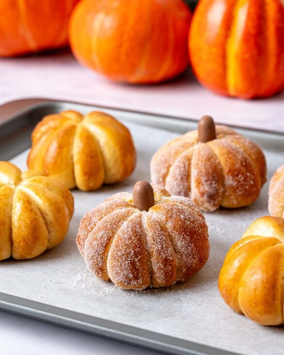 Pumpkin shaped buns covered in sugar on a baking tray.