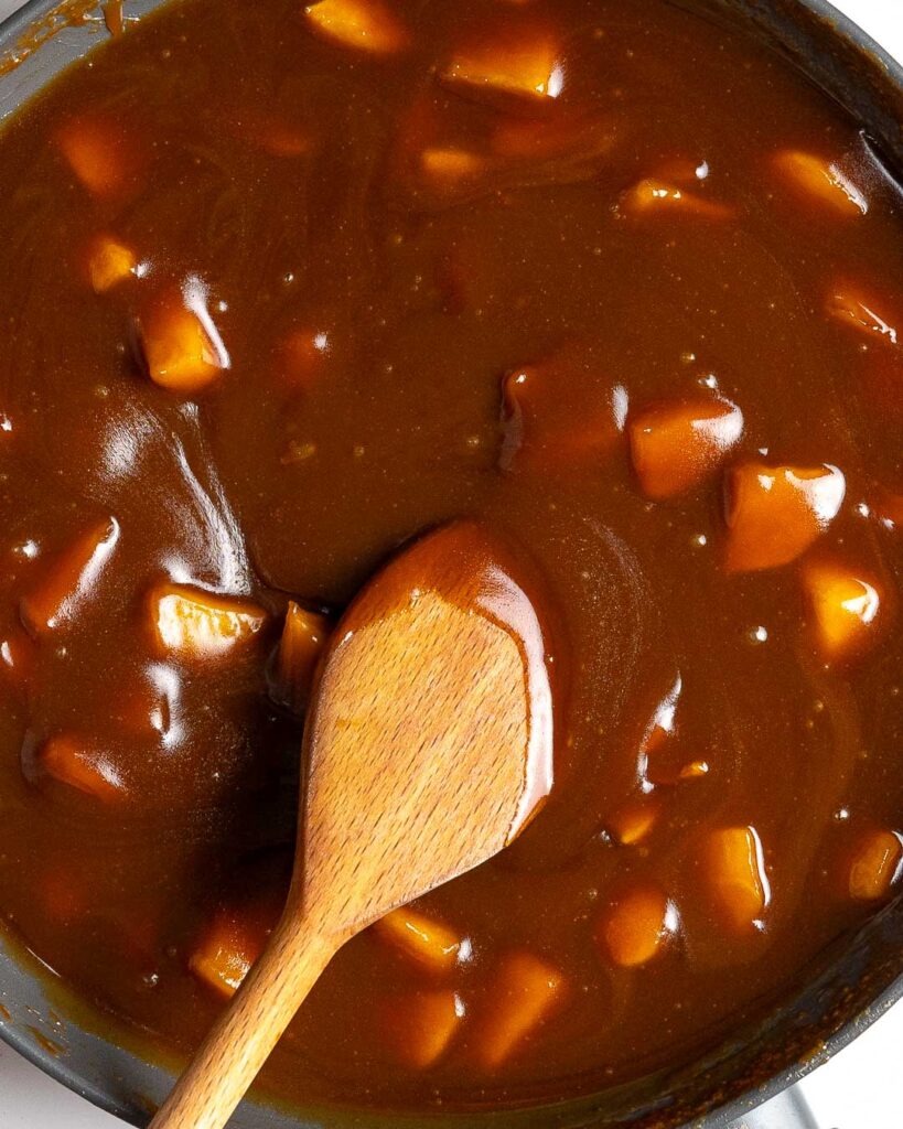 Apple caramel sauce in a sauce pan, being stirred with a wooden spoon.