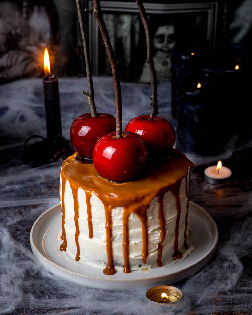 Carmel drip cake with three red candy apples on top.