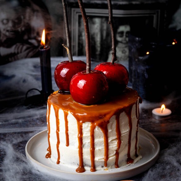 Caramel drip cake with three red candy apples on top.