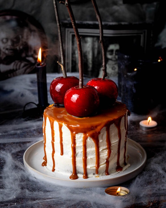 Caramel drip cake with three red candy apples on top.