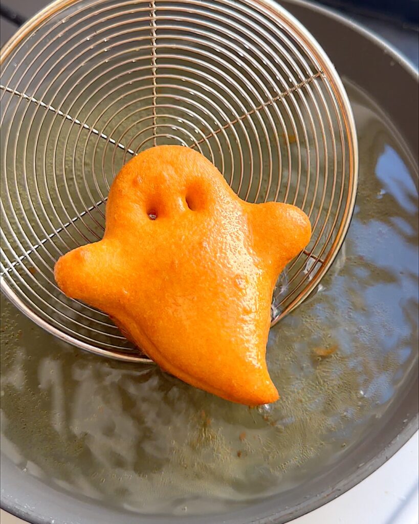 Ghost shaped beignet being removed from oil after being fried.