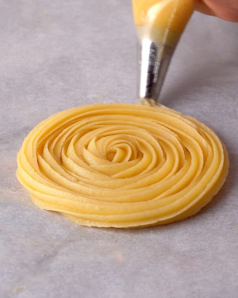 Churro disc being piped on baking sheet.