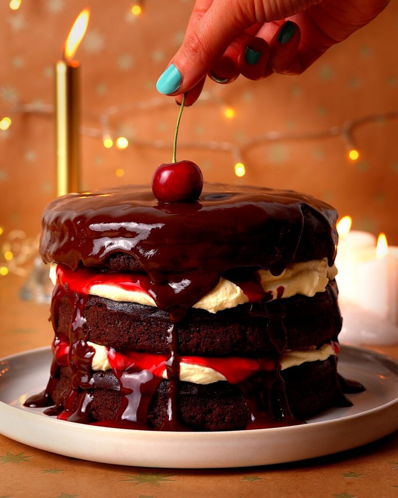 Cherry being placed on top of a black forest chocolate cake.