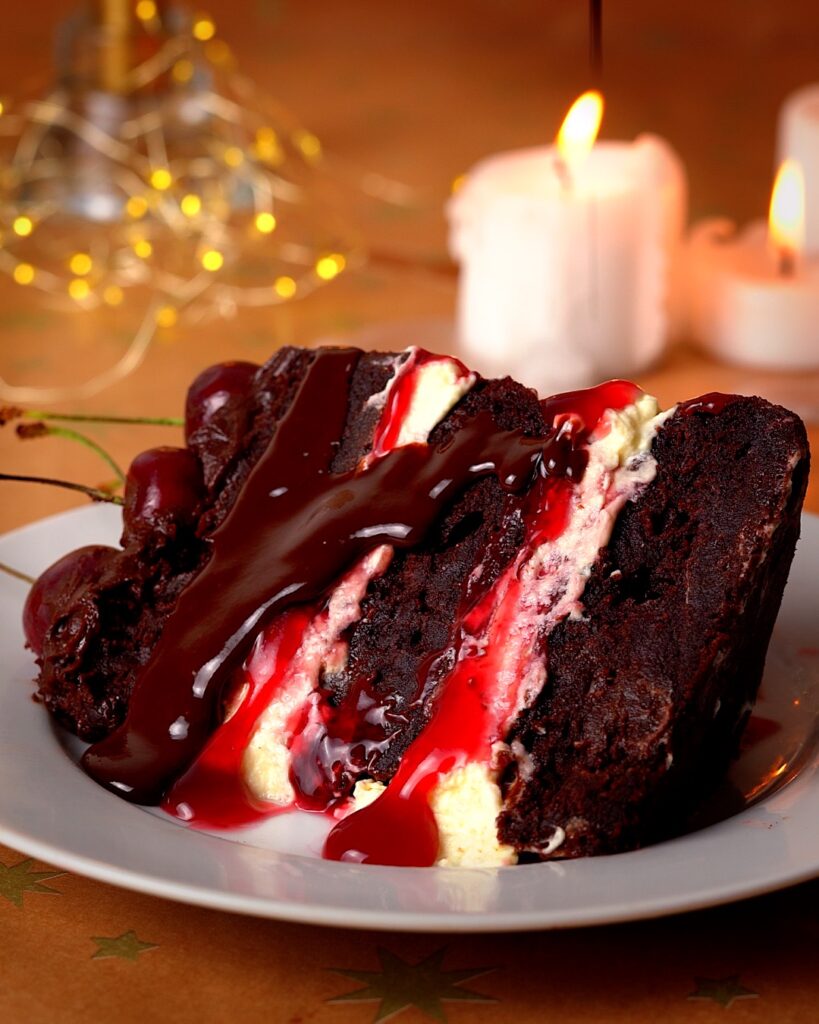 Slice of black forest chocolate cake with chocolate sauce drizzled on top.
