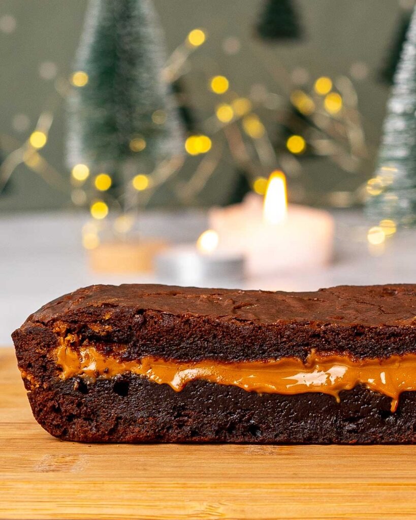 Biscoff stuffed brownie cut In half on a wooden board with Christmas lights in the background.