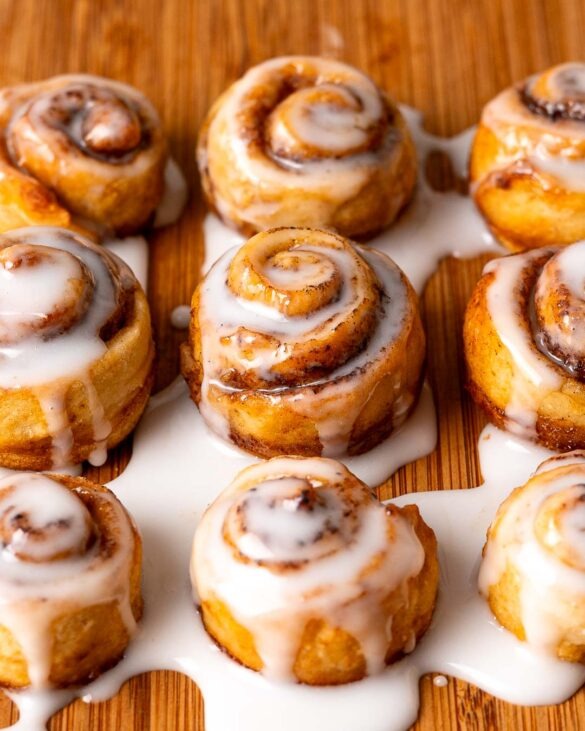 Mini cinnamon rolls drizzled in icing on a wood chopping board.