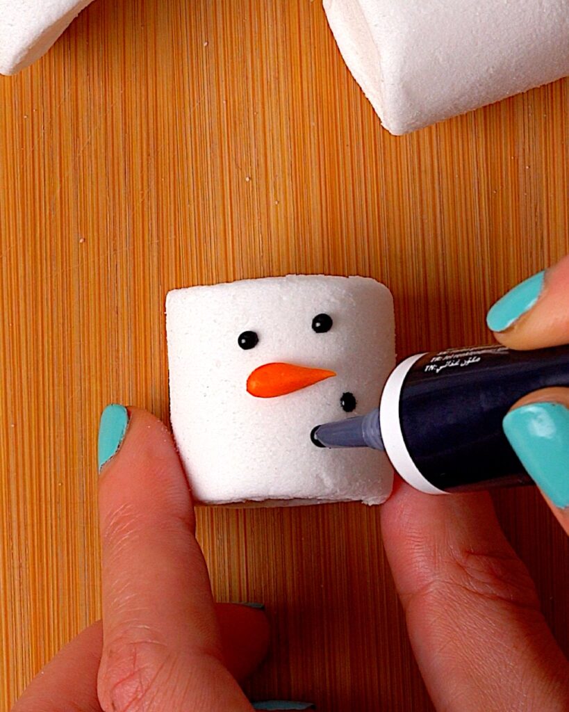 Marshmallow being decorated to look like a snowman head with black food colouring.