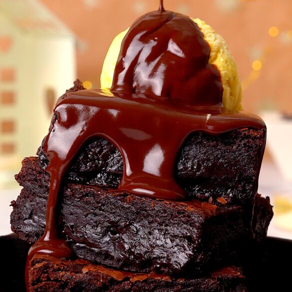 Fudgy brownie stack with chocolate sauce being poured on top.