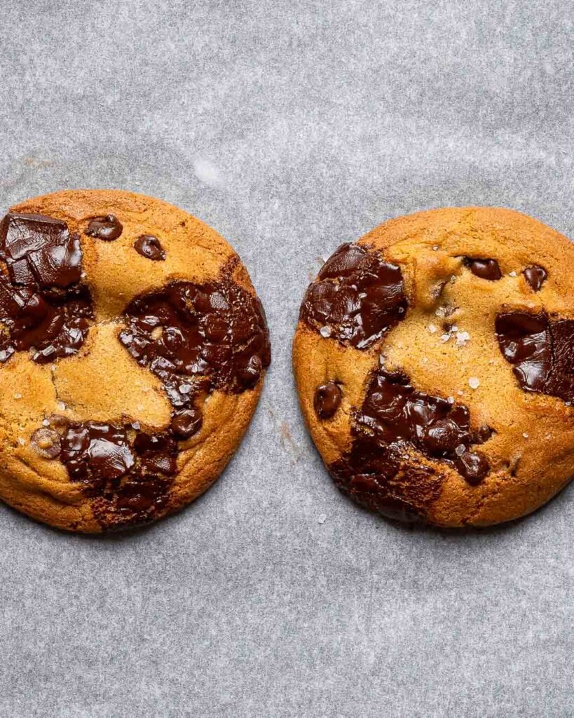 Two chocolate chip cookies on a baking tray.