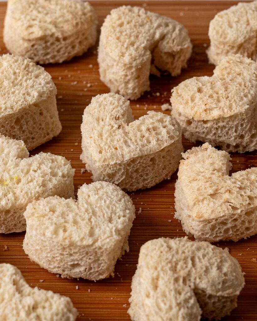 Heart shaped pieces of bread on a bread board.