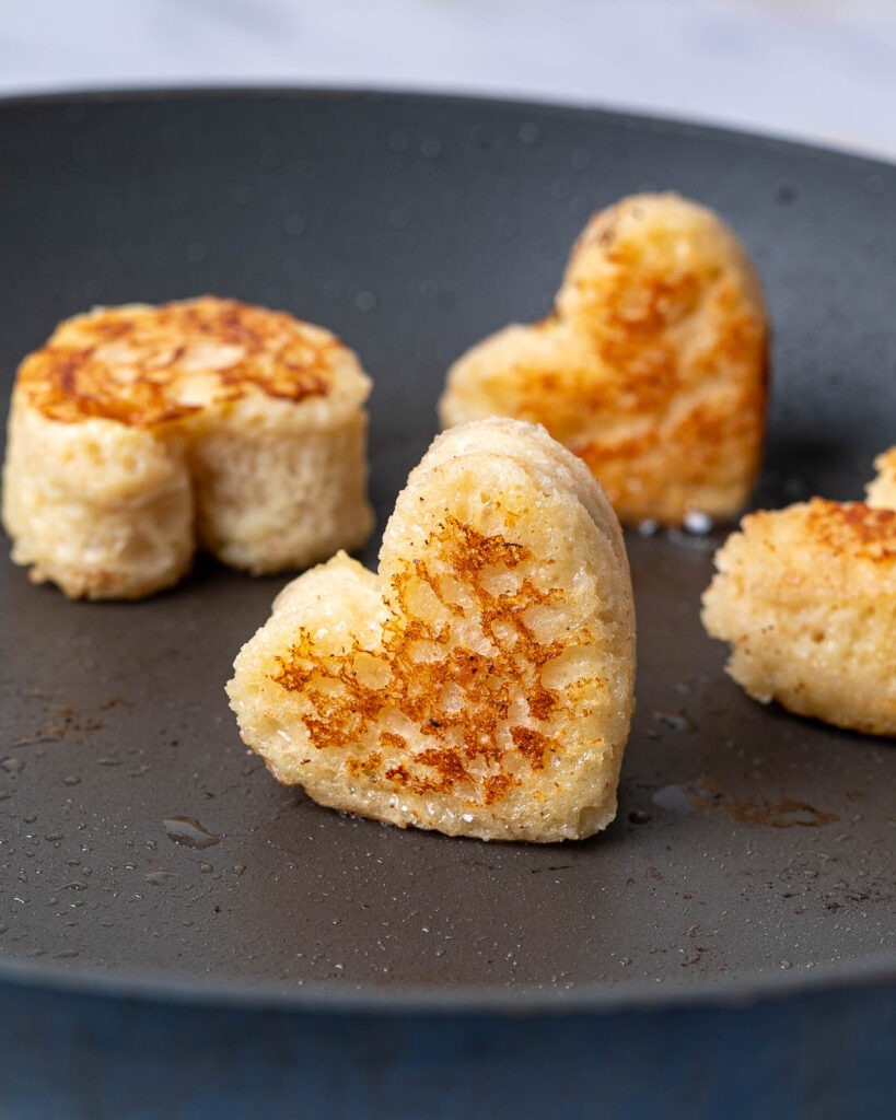 Heart shaped French toast bite in a frying pan.