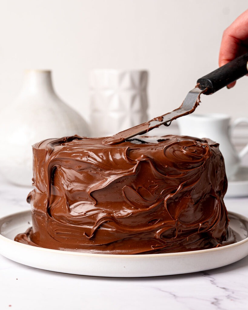 Chocolate cake being covered in Nutella with a spatula.