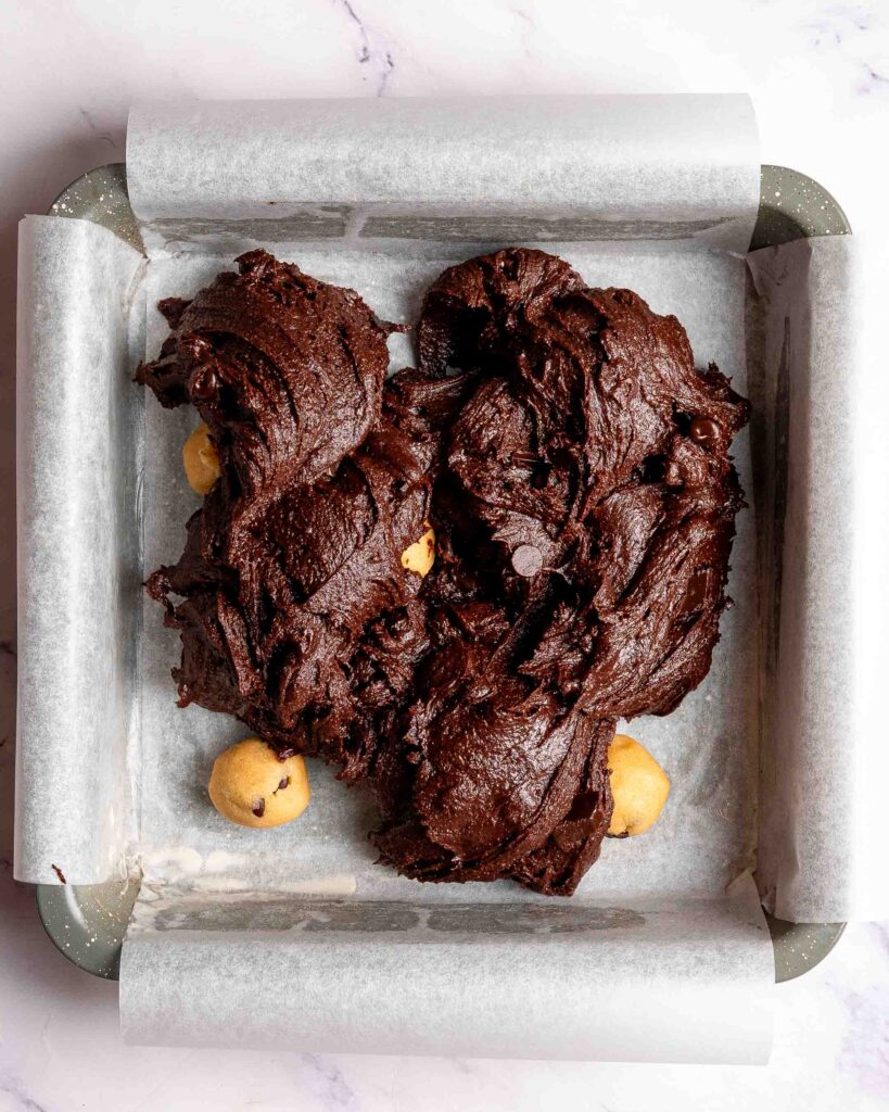 Brownie batter on top of cookie dough balls in brownie tin.