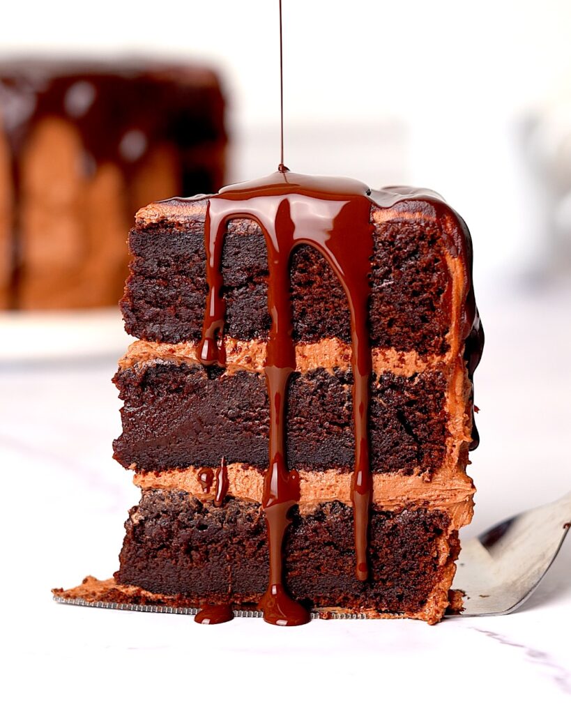 Slice of chocolate fudge cake with chocolate drip being poured on top.