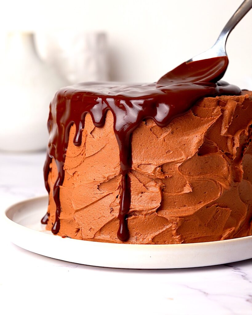 Chocolate drip being poured over a chocolate fudge cake.