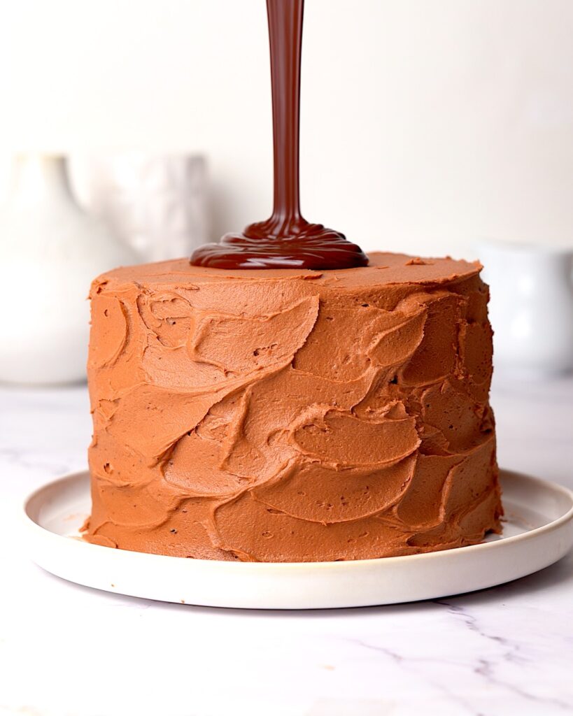 Chocolate drip being poured on top of a chocolate fudge cake.