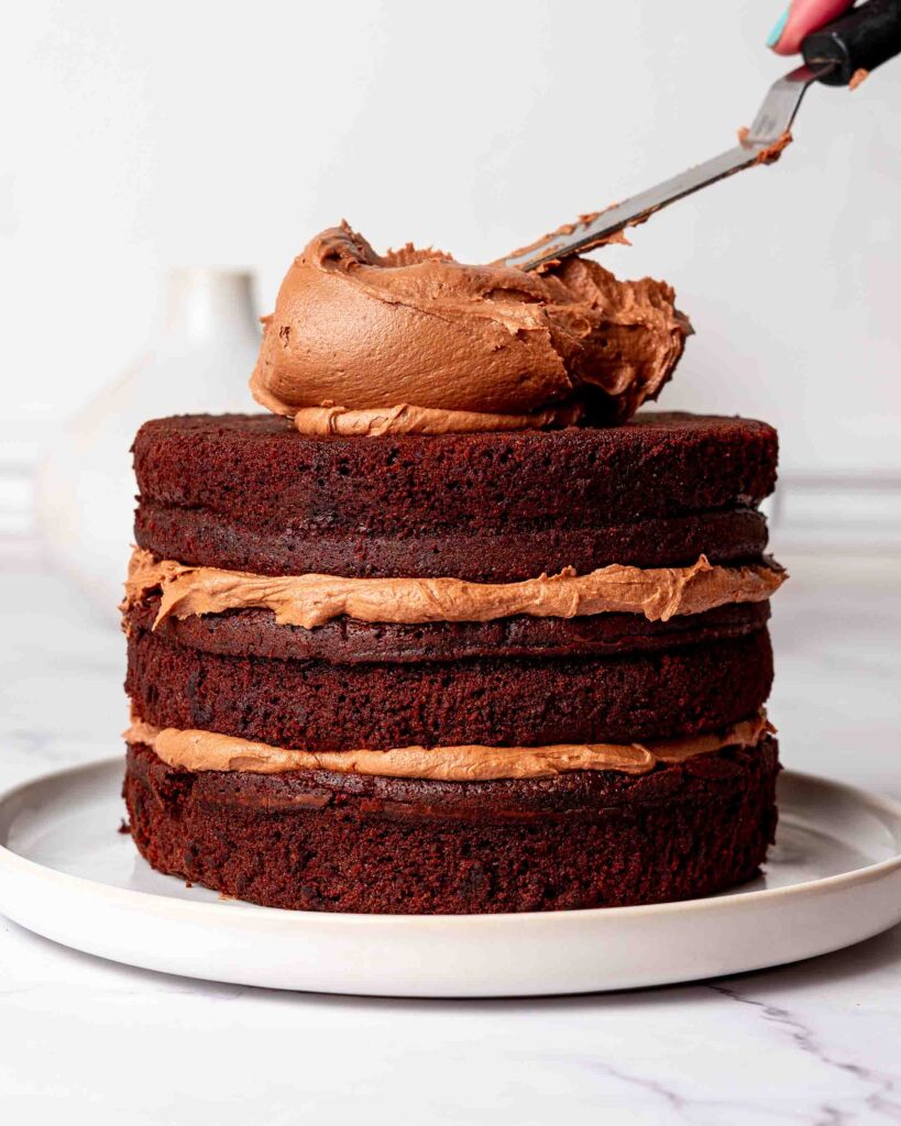 Chocolate buttercream being spread on a chocolate fudge cake.