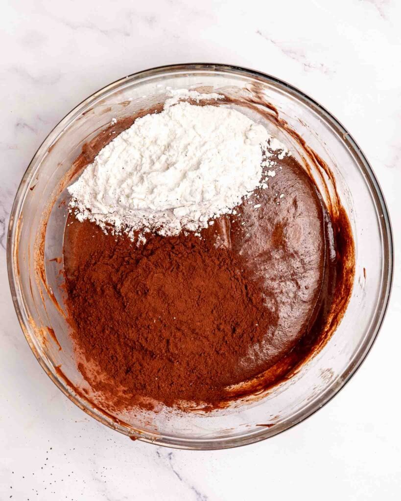 Dry ingredients added to brownie batter in a mixing bowl.