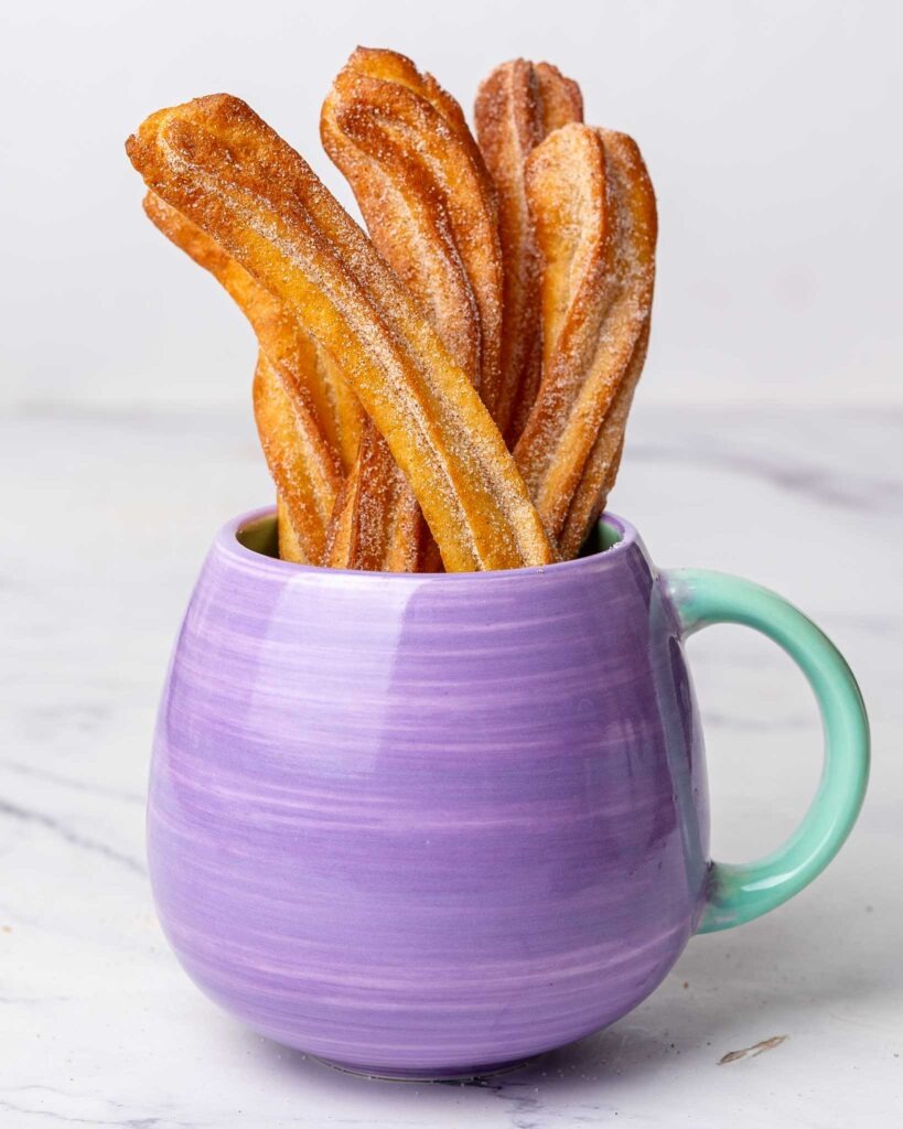 Air fryer churros in a lilac mug.