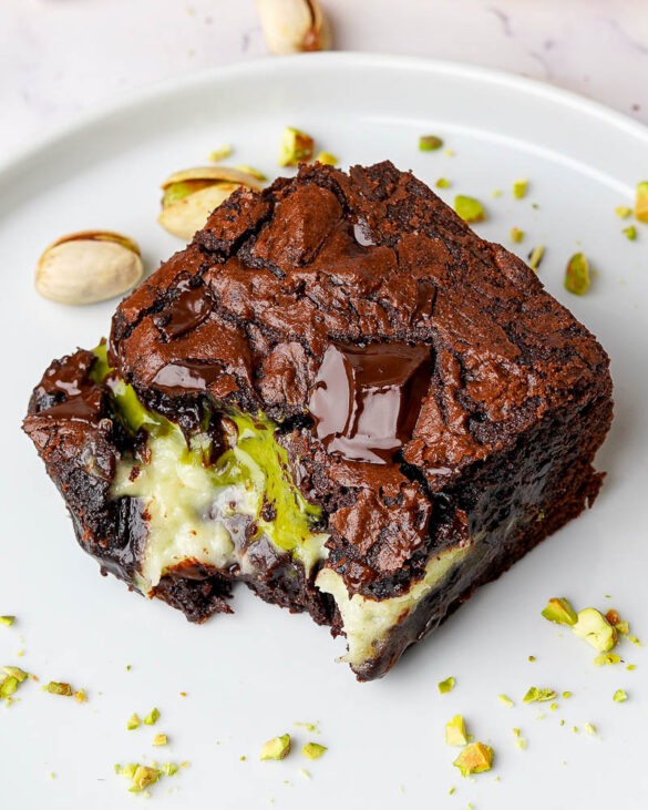 Pistachio cheesecake brownie with a bite taken out, revealing creamy white cheesecake filling and green pistachio cream inside