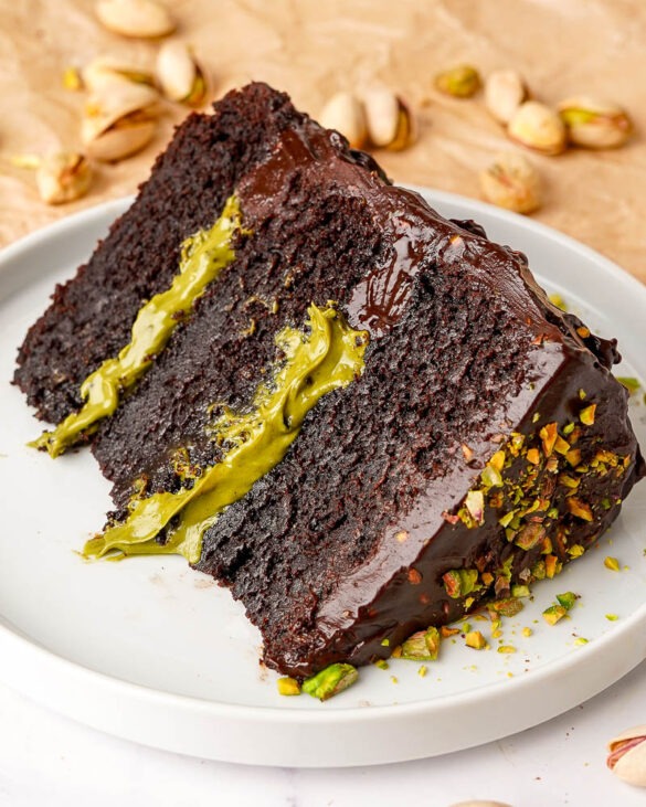 Three layer chocolate fudge cake with pistachio cream filling on a plate.