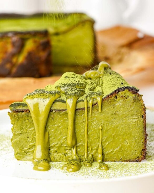 A slice of pistachio matcha Basque cheesecake on a plate, drizzled generously with creamy pistachio sauce