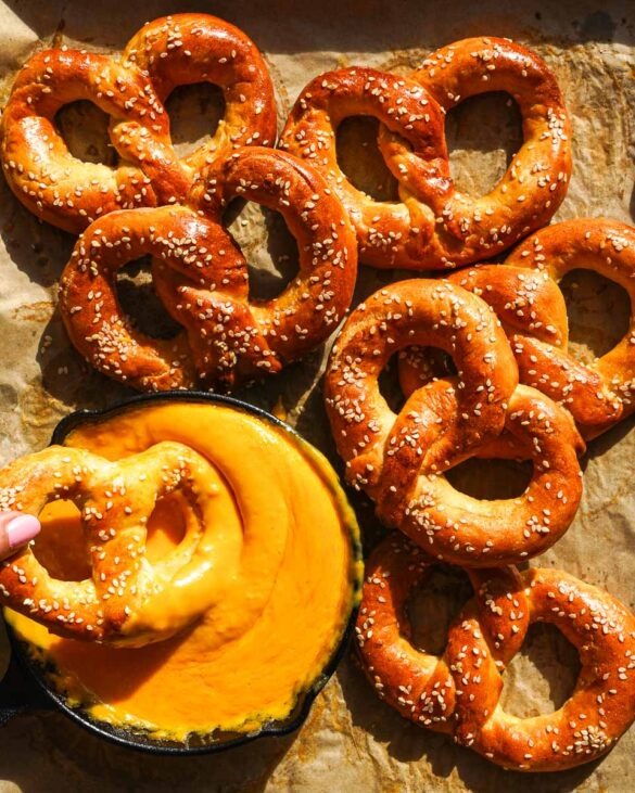 Pretzels on a tray with one being dipped in a cheese dip.