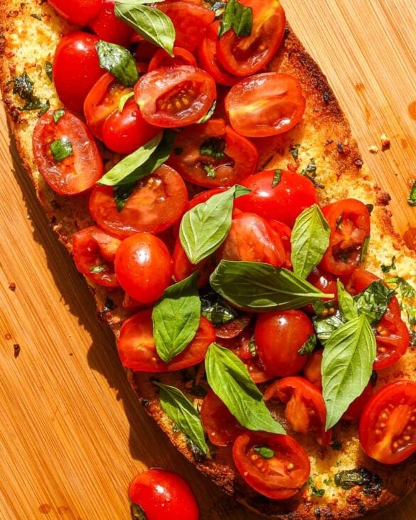 Bruschetta Garlic Bread on a board with basil leaves.