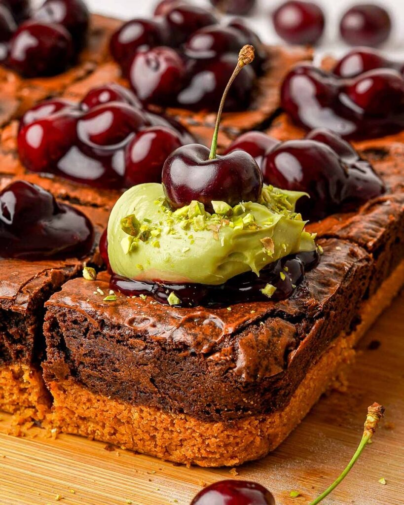 Pistachio cherry cheesecake brownies with spoonfuls pistachio cheesecake and fresh cherries on top.
