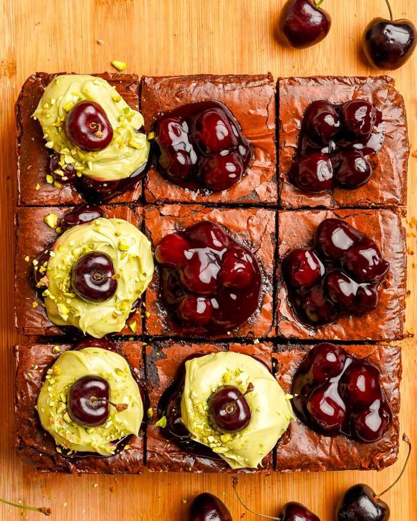 Pistachio cherry cheesecake brownies with spoonfuls pistachio cheesecake and fresh cherries on top.