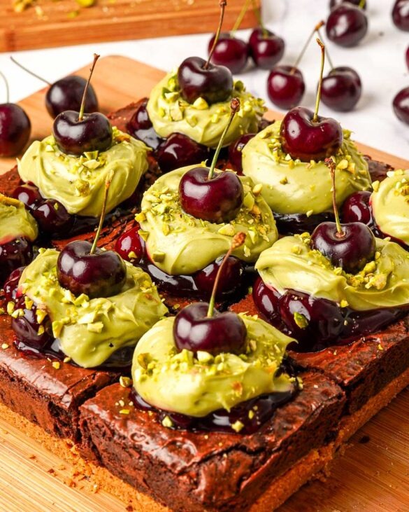 Pistachio cherry cheesecake brownies with spoonfuls pistachio cheesecake and fresh cherries on top.