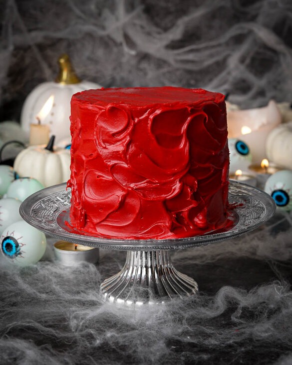 Mini red velvet cake with a messy red velvet cream cheese ganache on a silver cake stand.