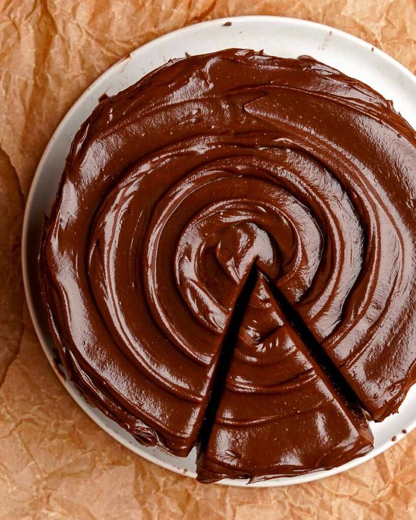 The top of a Six ingredient death by chocolate cake with a swirl of chocolate ganache and a slice cut.