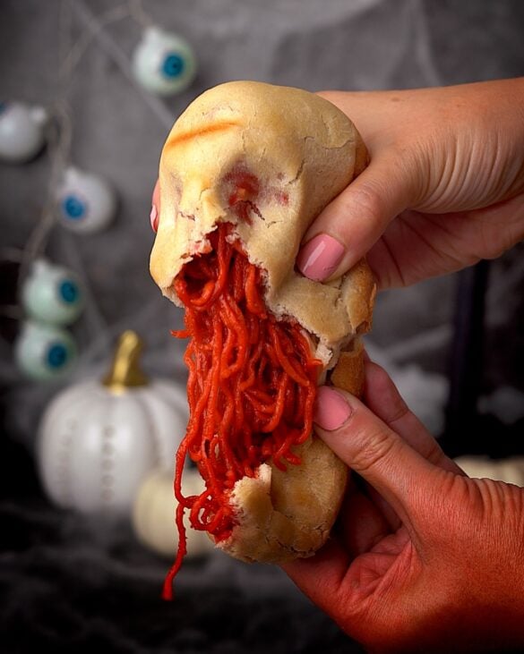 Pizza dough skulls being pulled apart to reveal red instant noodles for halloween.